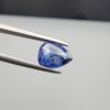 Studio close-up photographs showing the top table view with internal inclusions and reverse facet profile of a 1.41 carat pear cut natural blue sapphire loose gemstone held in precision tweezers.