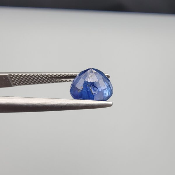 Studio close-up photographs showing the top table face and reverse natural mountain formation features of a 3.17 carat round cut natural blue sapphire loose gemstone held in precision tweezers.