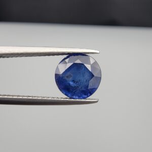 Studio close-up photographs showing the top table face and reverse natural mountain formation features of a 3.17 carat round cut natural blue sapphire loose gemstone held in precision tweezers.