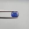 Studio close-up photographs showing the top table face with natural blackish internal inclusions and reverse facet profile of a 1.17 carat cushion cut natural blue sapphire loose gemstone held in precision tweezers.