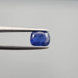 Studio close-up photographs showing the top table face with natural blackish internal inclusions and reverse facet profile of a 1.17 carat cushion cut natural blue sapphire loose gemstone held in precision tweezers.