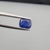 Studio close-up photographs showing the top table face with natural blackish internal inclusions and reverse facet profile of a 1.17 carat cushion cut natural blue sapphire loose gemstone held in precision tweezers.