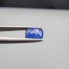 Studio close-up photographs showing the top table face with natural blackish internal inclusions and reverse facet profile of a 1.17 carat cushion cut natural blue sapphire loose gemstone held in precision tweezers.