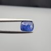 Studio close-up photographs showing the top table face with natural blackish internal inclusions and reverse facet profile of a 1.17 carat cushion cut natural blue sapphire loose gemstone held in precision tweezers.