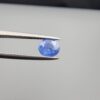 Studio close-up photographs showing the top table face and reverse facet profile of a 0.96 carat oval cut natural blue sapphire loose gemstone held in precision tweezers.