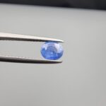 Studio close-up photographs showing the top table face and reverse facet profile of a 0.96 carat oval cut natural blue sapphire loose gemstone held in precision tweezers.