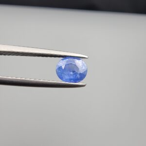 Studio close-up photographs showing the top table face and reverse facet profile of a 0.96 carat oval cut natural blue sapphire loose gemstone held in precision tweezers.