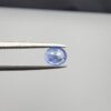 Studio close-up photographs showing the top table face and reverse facet profile of a 0.96 carat oval cut natural blue sapphire loose gemstone held in precision tweezers.