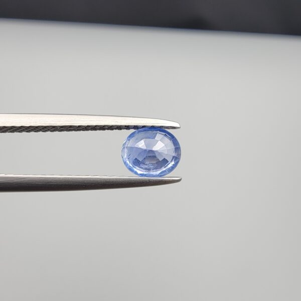 Studio close-up photographs showing the top table face and reverse facet profile of a 0.96 carat oval cut natural blue sapphire loose gemstone held in precision tweezers.