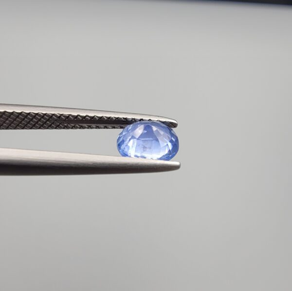 Studio close-up photographs showing the top table face and reverse facet profile of a 0.96 carat oval cut natural blue sapphire loose gemstone held in precision tweezers.