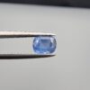 Studio close-up photographs showing the top table face and reverse facet profile of a 1.05 carat cushion cut natural blue sapphire loose gemstone held in precision tweezers.