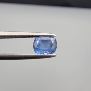 Studio close-up photographs showing the top table face and reverse facet profile of a 1.05 carat cushion cut natural blue sapphire loose gemstone held in precision tweezers.