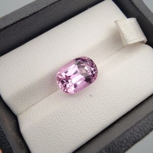 Studio close-up photograph showcasing a 6.67 carat cushion mixed cut natural kunzite loose gemstone resting securely inside a black display box with a white cushion lining.