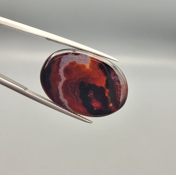 "Natural Carnelian Banded Agate Sulemani Aqeeq gemstone 25.08 carat oval cabochon from Iran held in tweezers showing brown, black, and white natural bands"