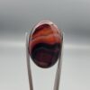"Natural Carnelian Banded Agate Sulemani Aqeeq gemstone 25.08 carat oval cabochon from Iran held in tweezers showing brown, black, and white natural bands"