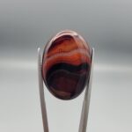 "Natural Carnelian Banded Agate Sulemani Aqeeq gemstone 25.08 carat oval cabochon from Iran held in tweezers showing brown, black, and white natural bands"