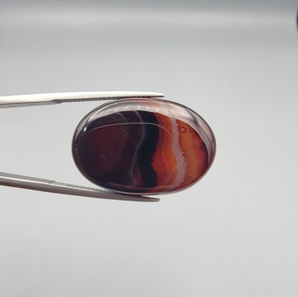 "Natural Carnelian Banded Agate Sulemani Aqeeq gemstone 25.08 carat oval cabochon from Iran held in tweezers showing brown, black, and white natural bands"