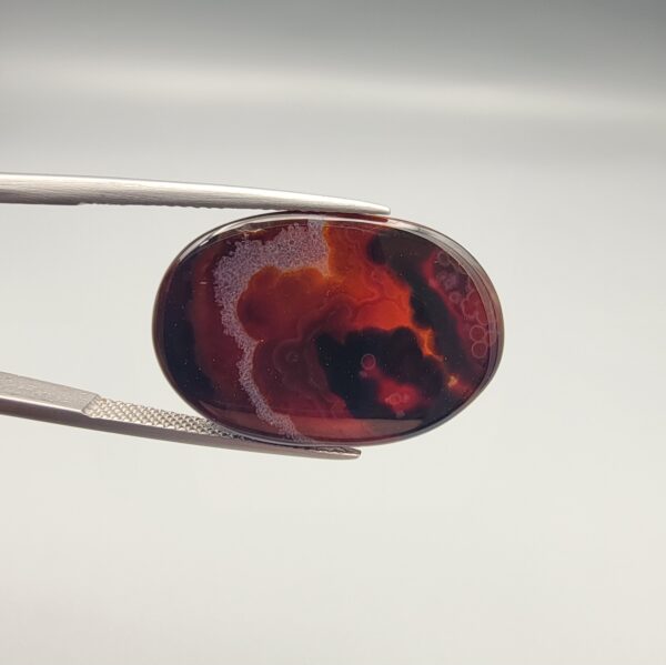 "Natural Carnelian Banded Agate Sulemani Aqeeq gemstone 25.08 carat oval cabochon from Iran held in tweezers showing brown, black, and white natural bands"