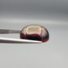 Studio close-up photographs showing the high-domed top surface, side profile, and reverse pattern views of a 17.43 carat oval cabochon natural multi-color agate loose gemstone held in precision tweezers.