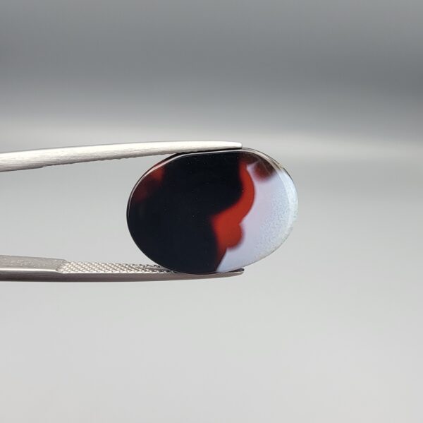 Studio close-up photographs showing the high-domed top surface, side profile, and reverse pattern views of a 17.43 carat oval cabochon natural multi-color agate loose gemstone held in precision tweezers.