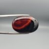 Studio close-up photographs showing the high-domed top surface, contrasting natural color bands, and reverse pattern views of a 25.48 carat oval cabochon natural banded agate loose gemstone held in precision tweezers.