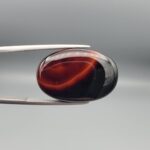 Studio close-up photographs showing the high-domed top surface, contrasting natural color bands, and reverse pattern views of a 25.48 carat oval cabochon natural banded agate loose gemstone held in precision tweezers.
