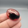 Studio close-up photographs showing the high-domed top surface, contrasting natural color bands, and finger-scale perspective views of a 60.66 carat oval cabochon natural Sulemani agate loose gemstone.