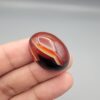 Studio close-up photographs showing the high-domed top surface, contrasting natural color bands, and finger-scale perspective views of a 60.66 carat oval cabochon natural Sulemani agate loose gemstone.