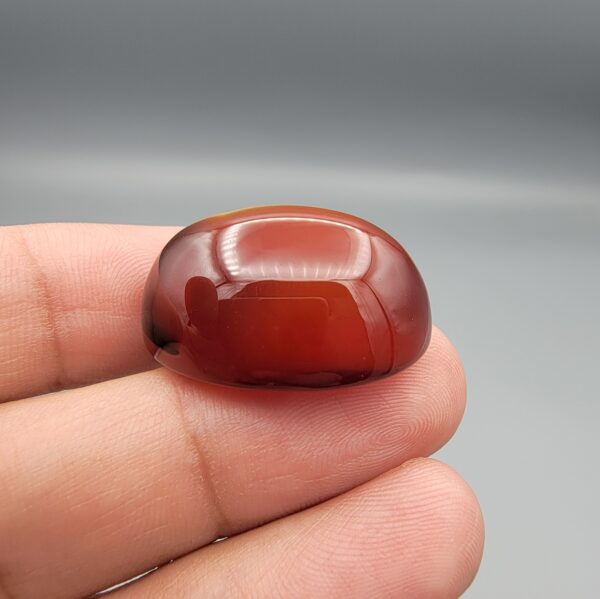 Studio close-up photographs showing the high-domed top surface, contrasting natural color bands, and finger-scale perspective views of a 60.66 carat oval cabochon natural Sulemani agate loose gemstone.