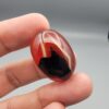 Studio close-up photographs showing the high-domed top surface, contrasting natural color bands, and finger-scale perspective views of a 60.66 carat oval cabochon natural Sulemani agate loose gemstone.