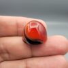 Studio close-up photographs showing the high-domed top surface, distinct natural multi-color banding, and finger-scale perspective views of a 34.28 carat dome-shaped natural carnelian Sulemani agate loose gemstone.