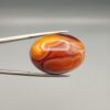 Studio close-up photographs showing the high-domed top surface, intricate concentric color banding, and reverse pattern views of a 56.58 carat dome-shaped natural chalcedony banded agate loose gemstone held in precision tweezers.