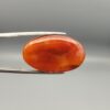 Studio close-up photographs showing the smooth polished dome, side profile featuring distinct internal black banding, and reverse pattern views of a 24.85 carat oval carnelian agate loose gemstone held in precision tweezers.