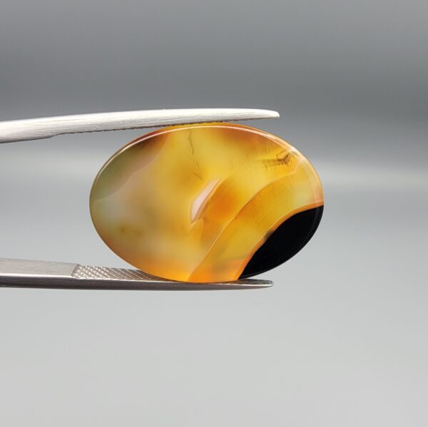 Studio close-up photographs showing the high-domed top surface, contrasting black and orange banding, and orientation views of a 21.68 carat oval cabochon natural chalcedony agate loose gemstone held in precision tweezers.
