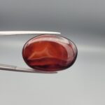 Studio close-up photographs showing the high-domed top surface, deep dark banding, and reverse pattern views of a 28.80 carat oval cabochon natural chalcedony agate loose gemstone held in precision tweezers.