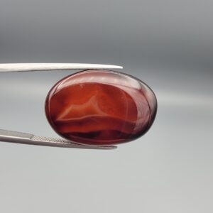 Studio close-up photographs showing the high-domed top surface, deep dark banding, and reverse pattern views of a 28.80 carat oval cabochon natural chalcedony agate loose gemstone held in precision tweezers.