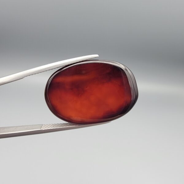 Studio close-up photographs showing the high-domed top surface, deep dark banding, and reverse pattern views of a 28.80 carat oval cabochon natural chalcedony agate loose gemstone held in precision tweezers.