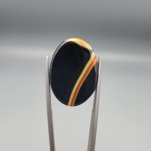 Studio close-up photographs showing the high-domed top surface, distinct natural "7" number pattern banding, and profile thickness views of a 21.69 carat oval cabochon Sulemani Aqeeq loose gemstone held in precision tweezers.