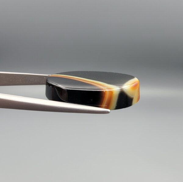 Studio close-up photographs showing the high-domed top surface, distinct natural "7" number pattern banding, and profile thickness views of a 21.69 carat oval cabochon Sulemani Aqeeq loose gemstone held in precision tweezers.