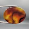 ​Studio close-up photographs showing the high-domed translucent top surface, intricate organic black and white banding formations, and reverse pattern views of a 49.55 carat oval cabochon orangish yellow agate loose gemstone held in precision tweezers.