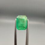 Studio close-up photograph showing the top-down view of a 1.49 carat octagonal emerald cut natural green emerald gemstone held securely in precision tweezers.