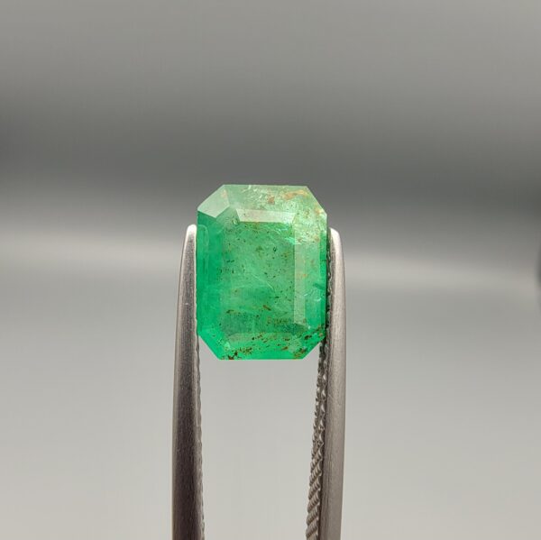 Studio close-up photograph showing the top-down view of a 1.49 carat octagonal emerald cut natural green emerald gemstone held securely in precision tweezers.