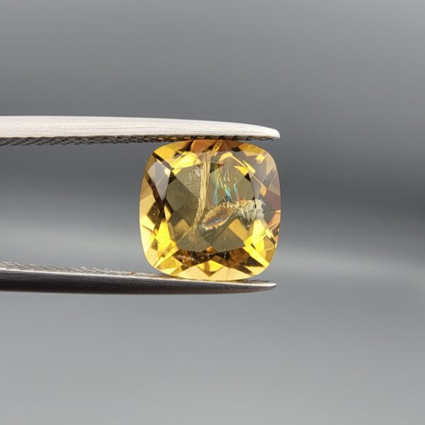 Studio close-up photographs showing the high-brilliance facet pattern, luminous golden body, and striking untreated internal rainbow light reflections of a 2.98 carat cushion cut natural citrine quartz loose gemstone held in precision tweezers.