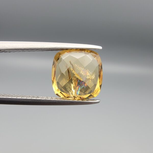 Studio close-up photographs showing the high-brilliance facet pattern, luminous golden body, and striking untreated internal rainbow light reflections of a 2.98 carat cushion cut natural citrine quartz loose gemstone held in precision tweezers.