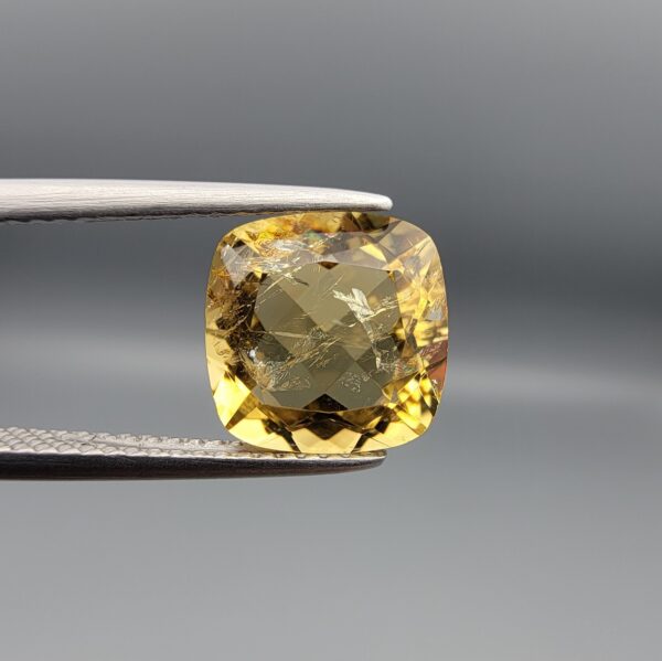 Studio close-up photographs showing the high-brilliance facet pattern, warm golden body, and striking natural internal needle crystal inclusions of a 2.93 carat cushion cut natural citrine quartz loose gemstone held in precision tweezers.
