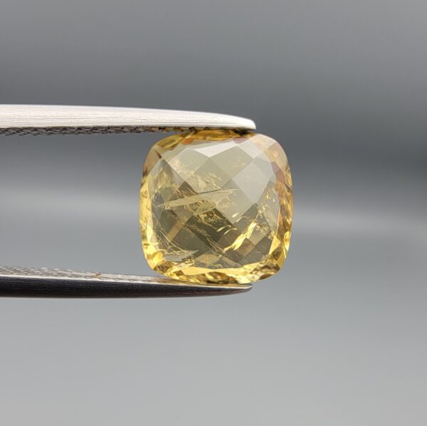 Studio close-up photographs showing the high-brilliance facet pattern, warm golden body, and striking natural internal needle crystal inclusions of a 2.93 carat cushion cut natural citrine quartz loose gemstone held in precision tweezers.