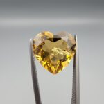 Studio close-up photographs showing the high-brilliance facet pattern, romantic heart outline, luminous golden body, and striking sparkling untreated internal crystal inclusions of a 5.68 carat heart shape natural citrine quartz loose gemstone held in precision tweezers.