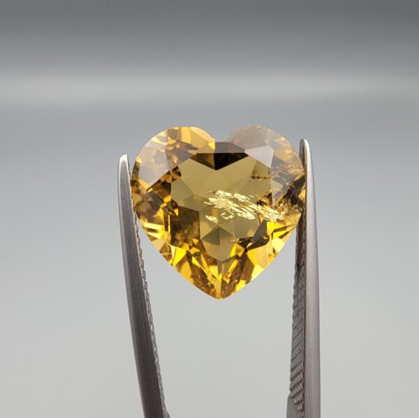 Studio close-up photographs showing the high-brilliance facet pattern, romantic heart outline, luminous golden body, and striking sparkling untreated internal crystal inclusions of a 5.68 carat heart shape natural citrine quartz loose gemstone held in precision tweezers.