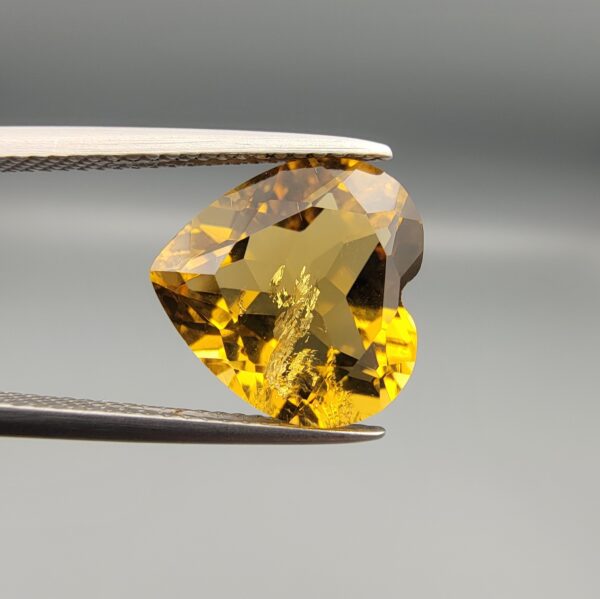Studio close-up photographs showing the high-brilliance facet pattern, romantic heart outline, luminous golden body, and striking sparkling untreated internal crystal inclusions of a 5.68 carat heart shape natural citrine quartz loose gemstone held in precision tweezers.