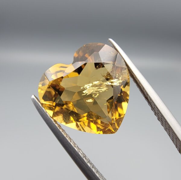 Studio close-up photographs showing the high-brilliance facet pattern, romantic heart outline, luminous golden body, and striking sparkling untreated internal crystal inclusions of a 5.68 carat heart shape natural citrine quartz loose gemstone held in precision tweezers.